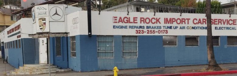 The hand painted sign along the blue block wall reading Eagle Rock Import Car Service, engine repairs, brakes, tune up, air conditioning, electrical